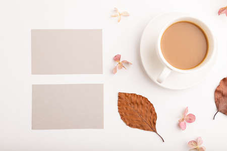 Composition with gray paper business card, brown beech autumn leaves, hydrangea flowers and cup of coffee. mockup on white background. Blank, flat lay, top view, still life, copy space.の写真素材