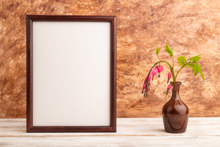 Wooden frame with pink dicentra, broken heart in ceramic vase on brown concrete background. side...