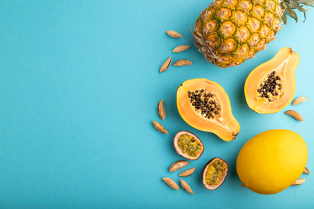 Ripe cut papaya, pineapple, melon, passion fruit, almonds on blue pastel background. Top view, flat lay, copy space. Tropical, healthy food, vacation, holidays concept.の写真素材