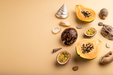 Ripe cut papaya, passion fruit, seashells, pebbles on orange pastel background. Side view, copy space. Tropical, healthy food, vacation, holidays concept.の写真素材