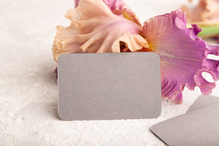 Gray business card with iris purple flowers on white concrete background. side view, copy space,...