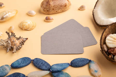 Brown paper business card with coconut, seashells, pebbles, beads on orange pastel background. Side view, copy space. Tropical, healthy food, vacation, holidays concept.の写真素材