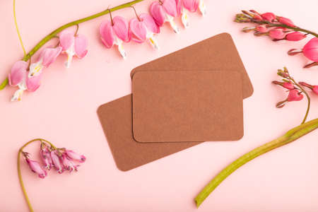 Brown business card with pink dicentra, broken heart flowers on pink pastel background. top view, flat lay, copy space, mockup, template, spring, summer minimalism concept.の写真素材
