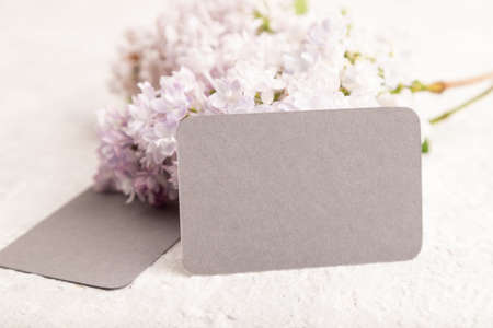 Gray business card with lilac flowers on gray concrete background. side view, copy space, mockup, template, spring, summer minimalism concept.の写真素材