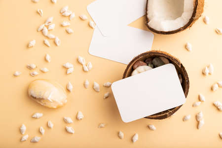 White paper business card with coconut and seashells on orange pastel background. Top view, flat lay, copy space. Tropical, healthy food, vacation, holidays concept.の写真素材
