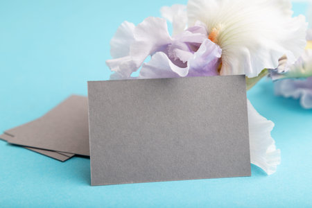 Gray business card with lilac iris flowers on blue pastel background. side view, copy space, still...