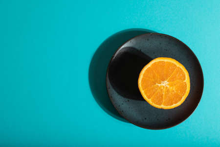 Ripe cut orange on blue ceramic plate on blue pastel background. Top view, flat lay, copy space, hard light. Tropical, healthy food, concept, minimalism.の写真素材