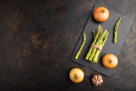 Bunch of fresh green asparagus, garlic, onion on slate board on black concrete background. Top view, flat lay, copy space. harvest, healthy, vegan food, concept.の写真素材