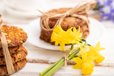 Oatmeal cookies with spring snowdrop flowers bluebells, narcissus and cup of coffee on white wooden background. side view, close up, defocused, still life. Breakfast, morning, spring concept.の写真素材