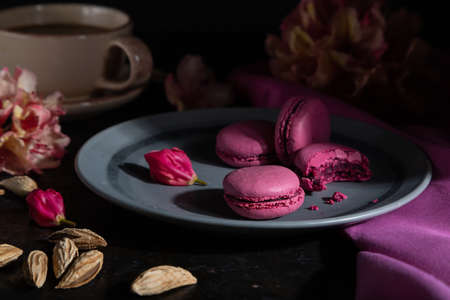 Purple macarons or macaroons cakes with cup of coffee on a black concrete background and pink textile. Hard light, low key. Side view, close up.の写真素材