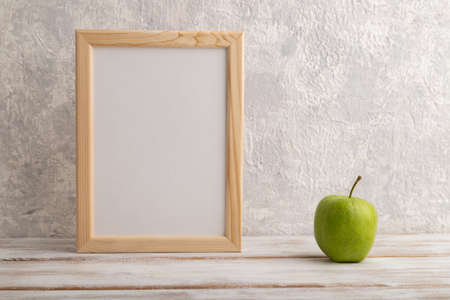 White wooden frame mockup with green apple on gray concrete background. Blank, vertical orientation, still life, copy space.の写真素材