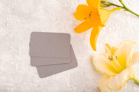 Gray paper business card mockup with orange day-lily flower on gray concrete background. Blank, top...