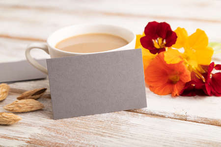 Gray paper business card mockup with orange nasturtium flower and cup of coffee on white wooden background. Blank, side view, copy space, still life. spring concept.の写真素材