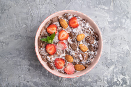 Chocolate cornflakes with milk, strawberry and almonds in ceramic bowl on gray concrete background....
