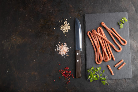 Traditional polish smoked pork sausage kabanos on a slate cutting board with salt and pepper on black concrete background. Top view, flat lay, copy space.の写真素材