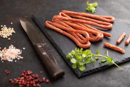 Traditional polish smoked pork sausage kabanos on a slate cutting board with salt and pepper on...