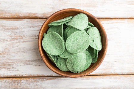green potato chips with herbs in wooden bowl on white wooden background. Top view, flat lay, copy space.の写真素材