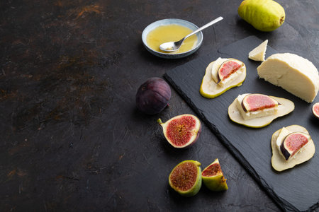 Summer appetizer with pear, cottage cheese, figs and honey on slate board on a black concrete...