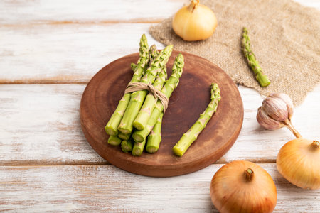 Bunch of fresh green asparagus, garlic, onion on white wooden background. Side view, close up. harvest, healthy, vegan food, concept.の写真素材