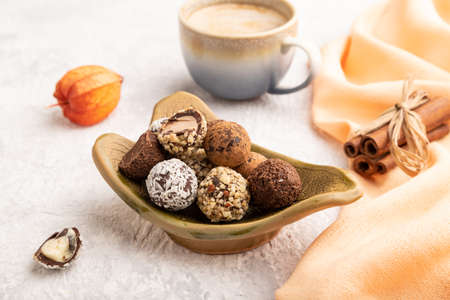 Chocolate truffle candies with cup of coffee on a gray concrete background and orange textile. side view, close up.の写真素材