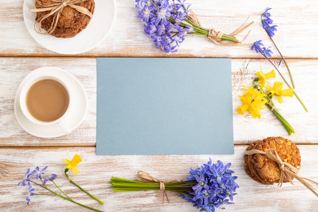 Blue paper sheet with oatmeal cookies, spring snowdrop flowers bluebells, narcissus and cup of...