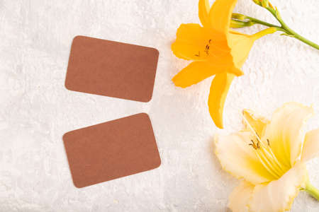 Brown paper business card mockup with orange day-lily flower on gray concrete background. Blank, top view, copy space, still life. spring concept.の写真素材
