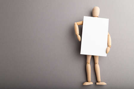Wooden mannequin holding blank poster on gray pastel background. copy space, isolated, presentation concept.の写真素材
