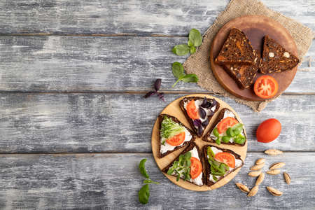Grain rye bread sandwiches with cream cheese, tomatoes and microgreen on gray wooden background and linen textile. top view, flat lay, copy space.の写真素材