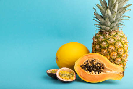 Ripe cut papaya, pineapple, melon, passion fruit, on blue pastel background. Side view, copy space. Tropical, healthy food, vacation, holidays concept.の写真素材