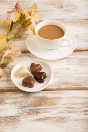 Cup of cioffee with chocolate candies, lilac and purple iris flowers on white wooden background. side view, flat lay, close up, still life. Breakfast, morning, spring concept.の写真素材