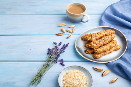 Crumble cookies with seasme and almonds on ceramic plate with cup of coffee and blue linen textile...