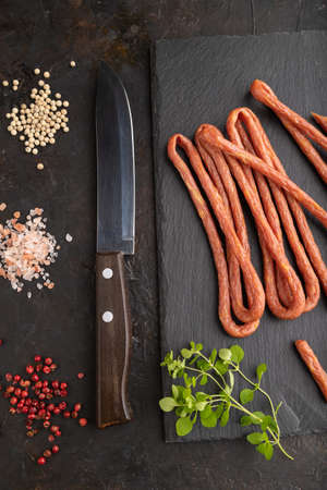 Traditional polish smoked pork sausage kabanos on a slate cutting board with salt and pepper on black concrete background. Top view, flat lay, close up.の写真素材