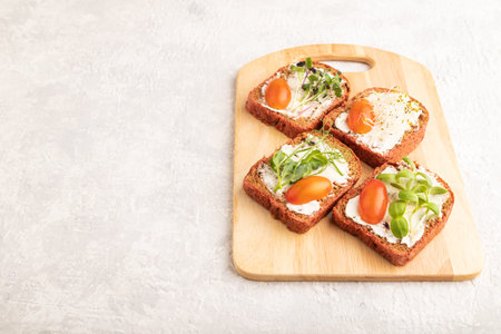 Red beet bread sandwiches with cream cheese, tomatoes and microgreen on gray concrete background....