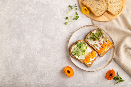 White bread sandwiches with cream cheese, calendula petals and microgreen on gray concrete...