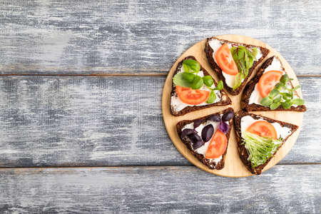 Grain rye bread sandwiches with cream cheese, tomatoes and microgreen on gray wooden background. top view, flat lay, copy space.の写真素材