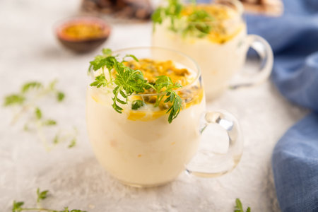 Yogurt with passionfruit and marigold microgreen in glass on gray concrete background with blue linen textile. Side view, close up, selective focus.の写真素材
