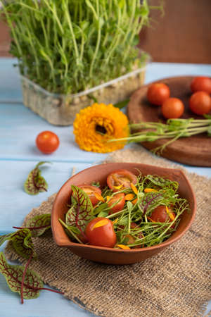 Vegetarian vegetables salad of tomatoes, marigold petals, microgreen sprouts on blue wooden background and linen textile. Side view, close up, selective focus.の写真素材