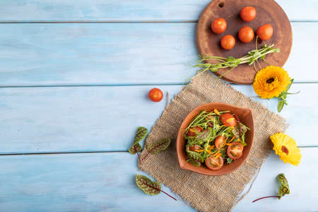 Vegetarian vegetables salad of tomatoes, marigold petals, microgreen sprouts on blue wooden background and linen textile. Top view, flat lay, copy space.の写真素材