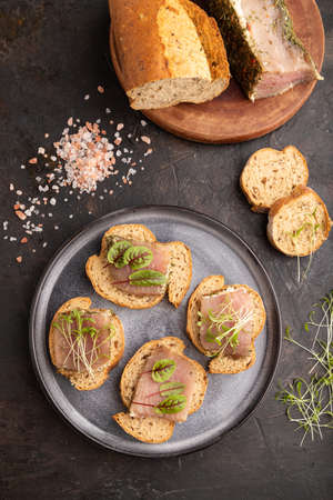 Bread sandwiches with jerky salted meat, sorrel and cilantro microgreen on black concrete background. top view, flat lay, close up.の写真素材