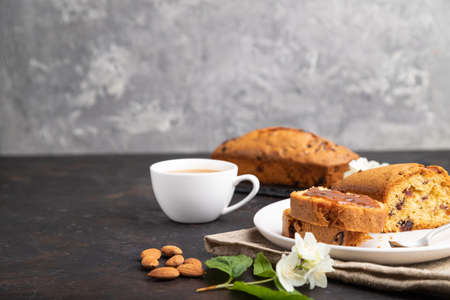 Homemade cake with raisins, almonds, soft caramel and a cup of coffee on a black concrete background and linen textile. Side view, copy space, selective focus.の写真素材