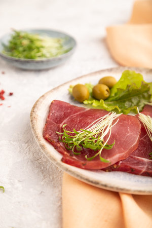 Slices of smoked salted meat with cilantro microgreen on gray concrete background and orange textile. Side view, close up, selective focus.の写真素材