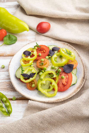 Vegetarian salad from green pea, tomatoes, pepper and basil on white wooden background and linen textile. side view, close up.の写真素材