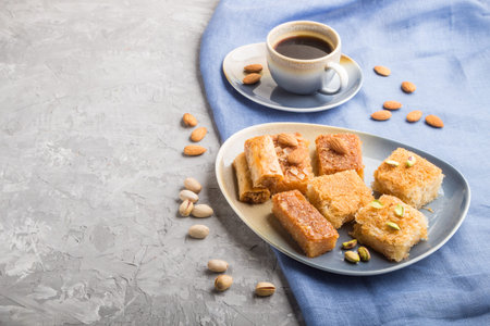 traditional arabic sweets (basbus, kunafa, baklava) and a cup of coffee on a gray concrete...