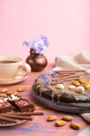 Homemade chocolate brownie cake with caramel cream and almonds with cup of coffee on a colored and pink background and linen textile. Side view, copy space, selective focus.の写真素材