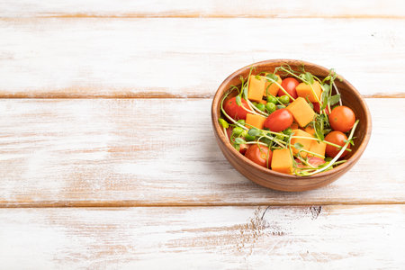 Vegetarian vegetable salad of tomatoes, pumpkin, microgreen pea sprouts on white wooden background. Side view, copy space, close up.