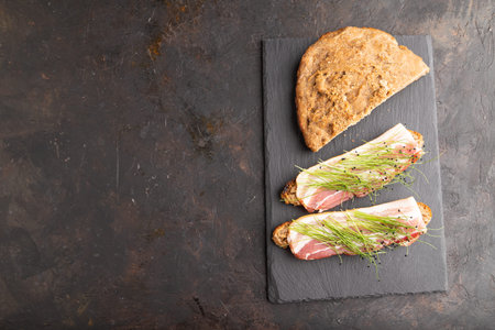Bread sandwiches with jerky salted meat and lard with onion microgreen on black concrete background....