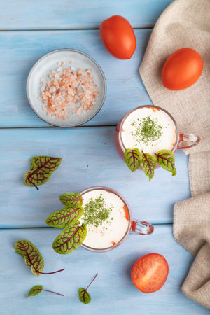 Tomato juice with sorrel, himalayan salt and sour cream in glass on blue wooden background with linen textile. Healthy drink concept. Top view, flat lay, close up.の写真素材