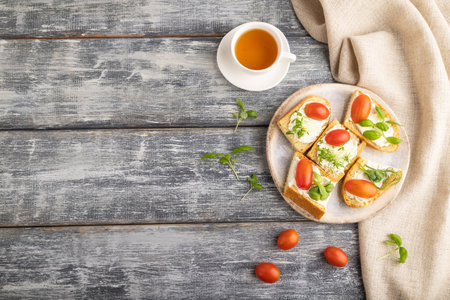 White bread sandwiches with cream cheese, tomatoes and microgreen on gray wooden background and...