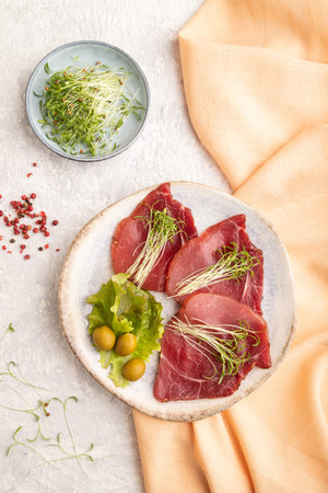 Slices of smoked salted meat with cilantro microgreen on gray concrete background and orange...