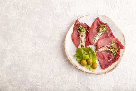 Slices of smoked salted meat with cilantro microgreen on gray concrete background. Top view, flat lay, copy space.の写真素材